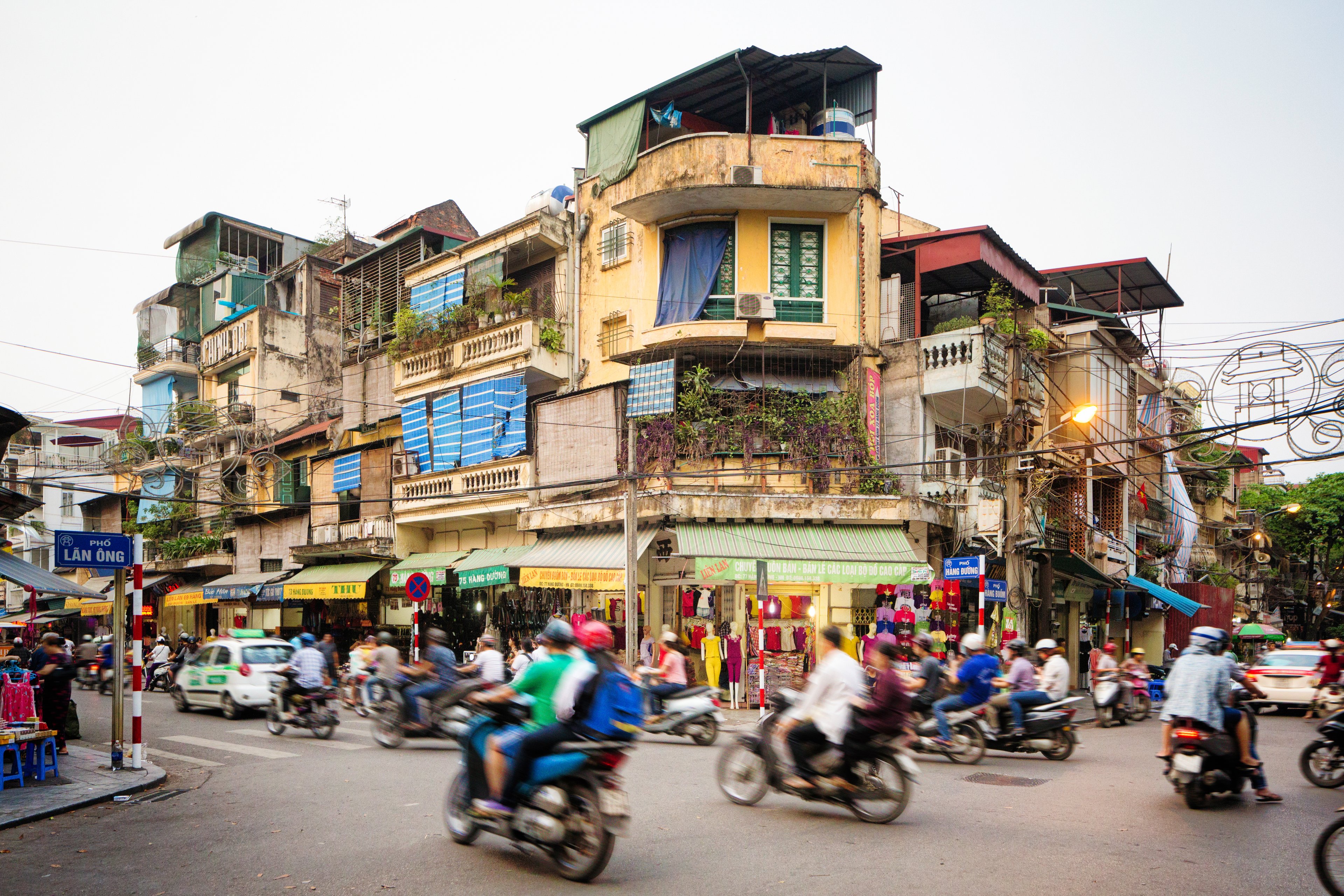 A busy street corner in Old Town Hanoi, North Vietnam, with motorbikes, cars, and shopfronts