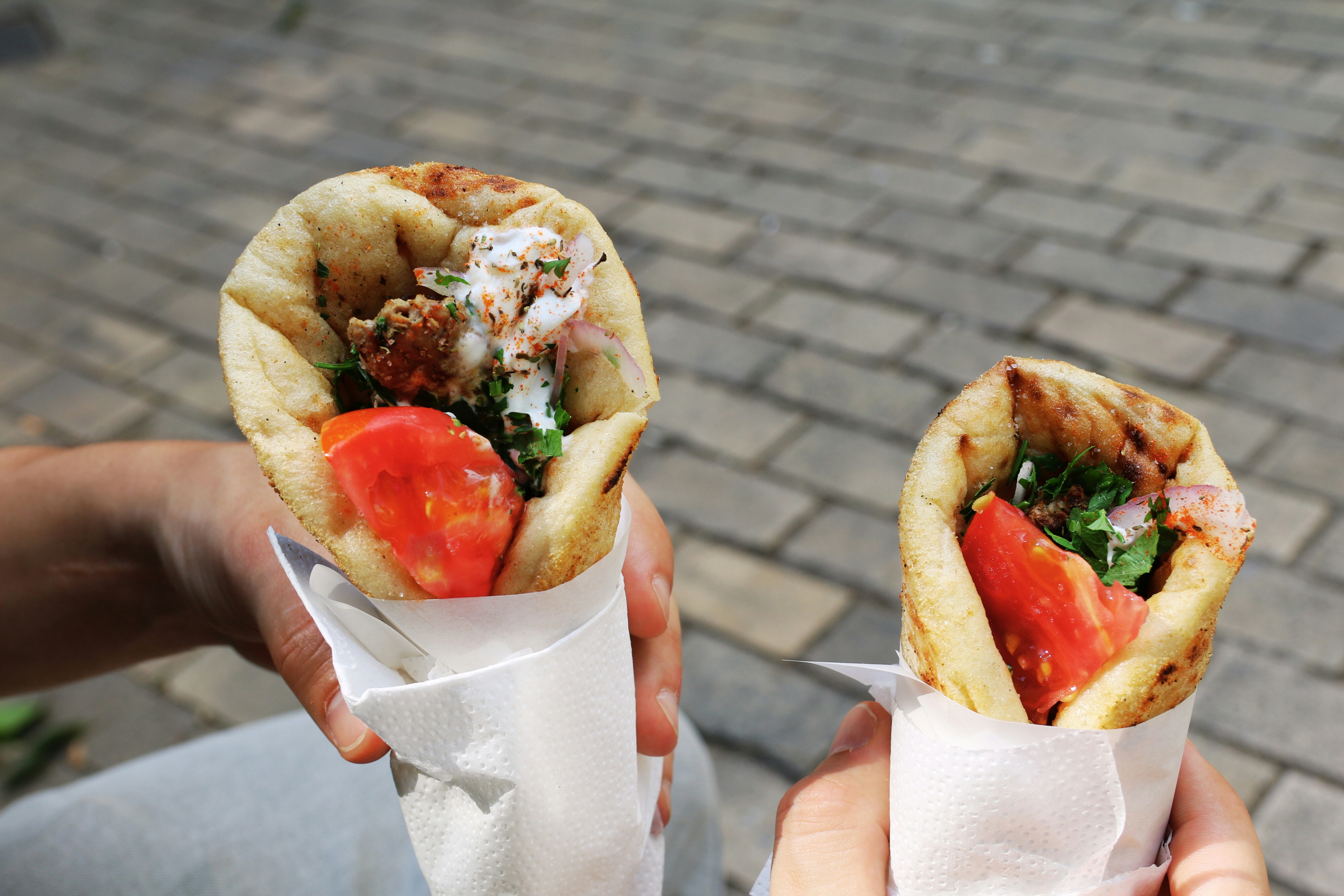 Person holding two Greek souvlakia with grilled meat and salad filling, typical Greek street food