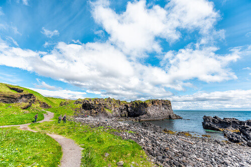 Tourists on a landscape trail, hiking with a view of the rocky beach in Hellnar National Park.