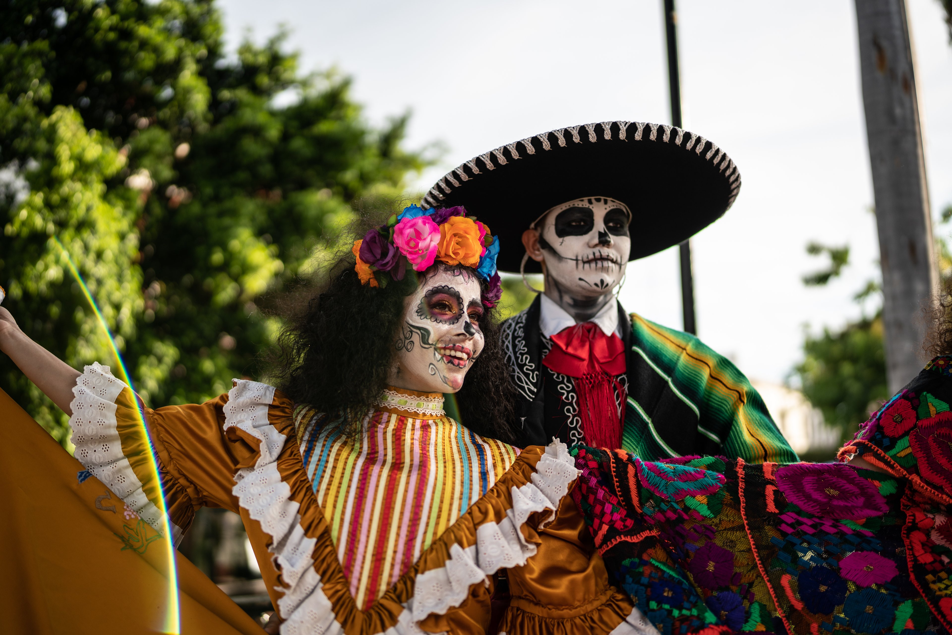 A couple wearing traditional Day of the Dead makeup with skull face paint, dressed in vibrant Mexican clothing during festival celebrations.