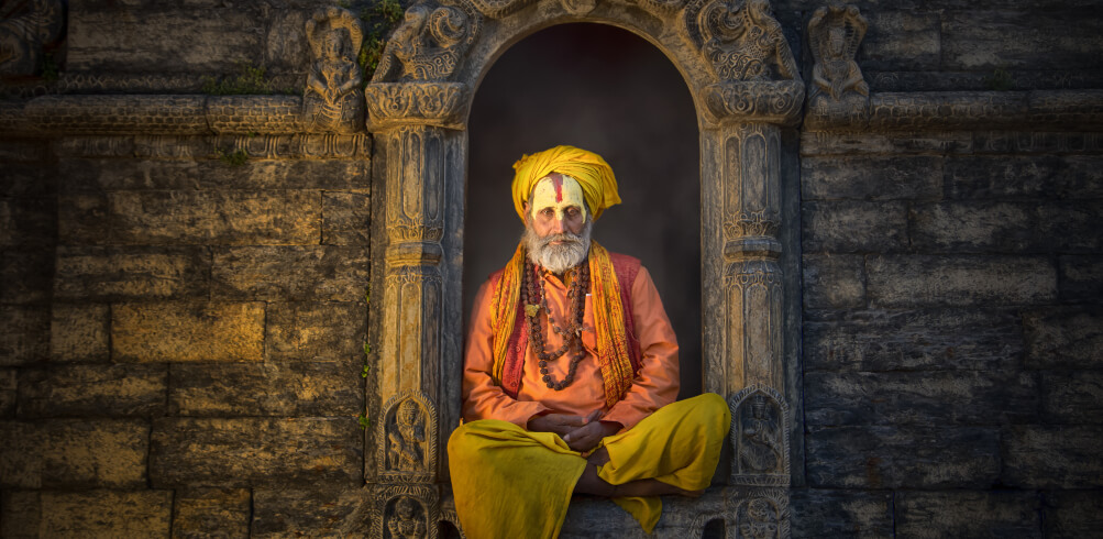 A Sadhu man with a painted face offers blessings at Pashupatinath Temple