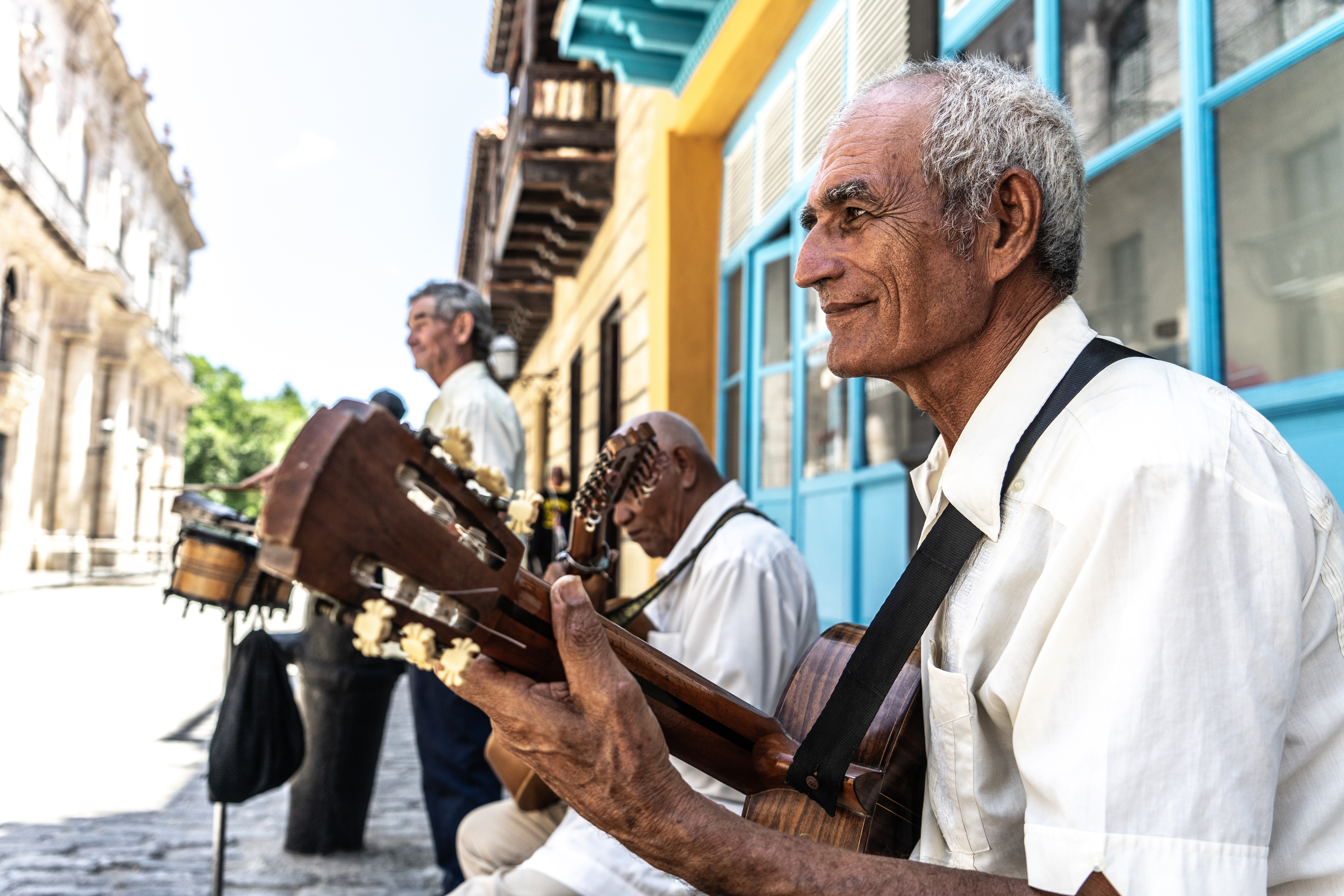 A senior man playing the guitar outdoors, adding to the local music scene and atmosphere