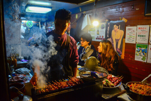 A tiny food stall in Omoide Yokocho, Shinjuku District, where a Japanese man grills tasty BBQ for customers.