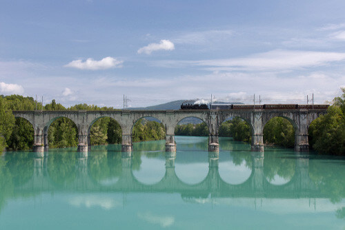 An Italian steam train passes over a stone arch bridge.