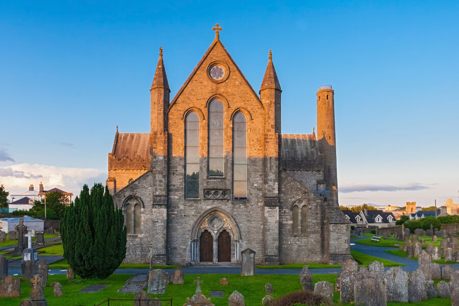 St. Canice Cathedral or the Kilkenny Cathedral at sunset with gravestones visible.