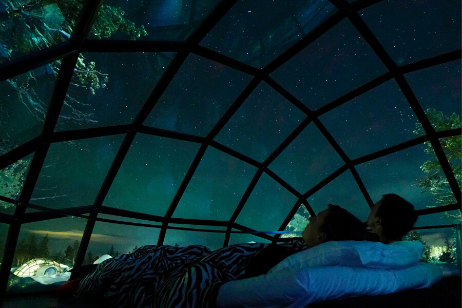 A couple admiring the aurora borealis at the glass igloo in Kakslauttanen Arctic Resort