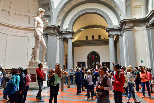 Tourists watch and photograph the statue of David.