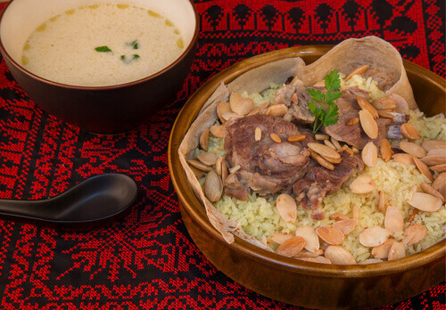 Mansaf: A Jordanian food featuring lamb, rice, and jameed yoghurt, traditionally served on a large platter with nuts and herbs.