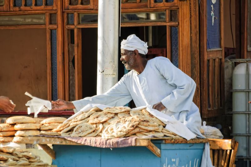 Bread seller handing a bread to a customer on the street.
