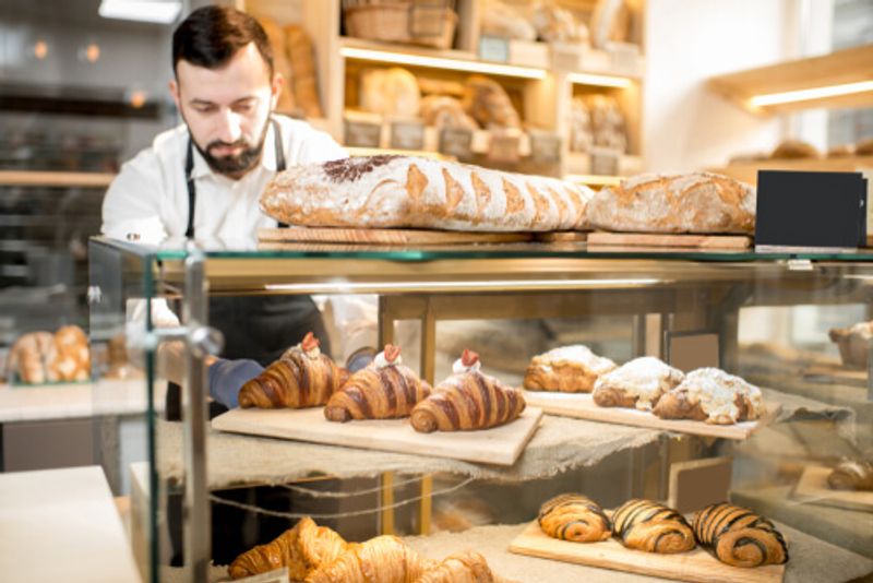 A shop worker stands before an impressive selection of pastries.