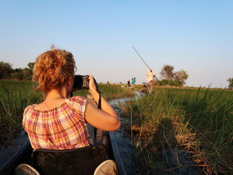 Tourist relaxing and taking pictures during a mokoro boat trip at the Okavango Delta.