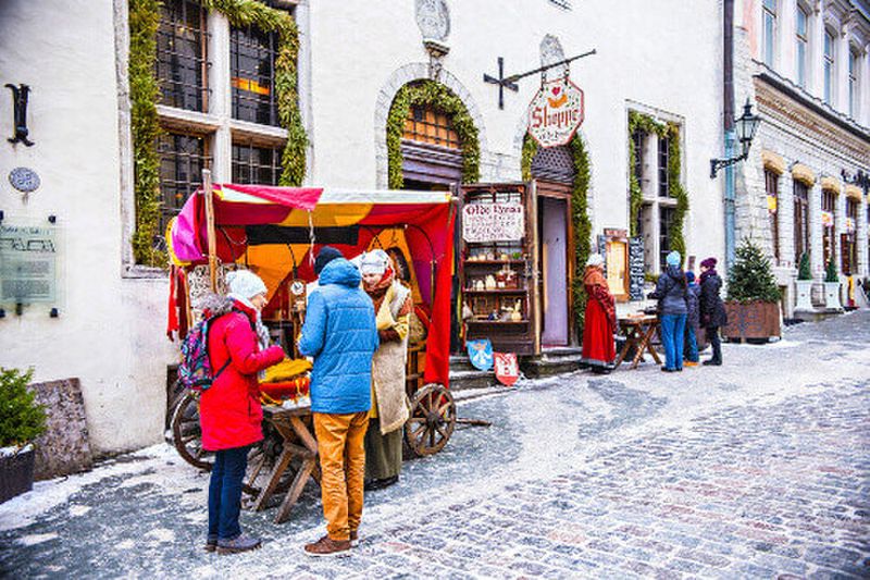 Estonian woman dressed in traditional medieval costume treating people with sweets at the central square of old Tallinn.