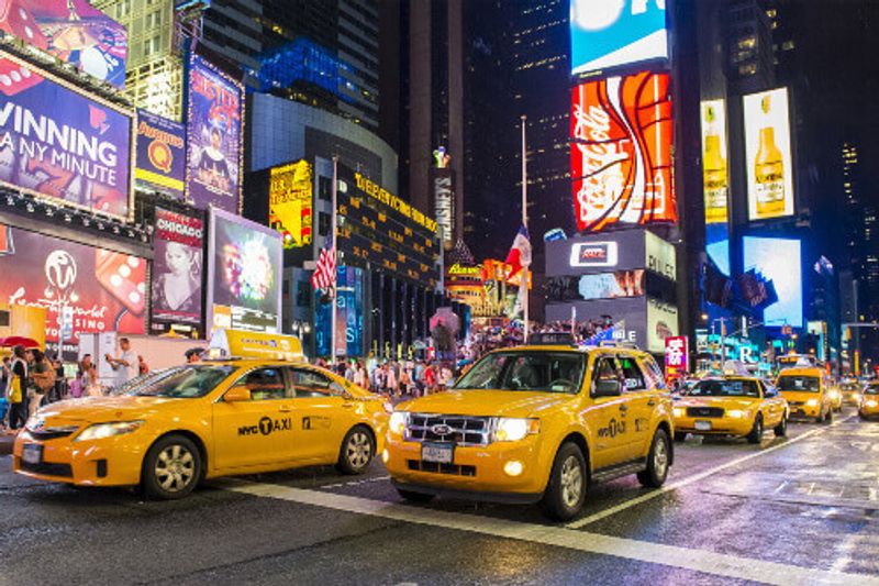 Times Square yellow cabs with neon ads for broadway shows and products in the background.
