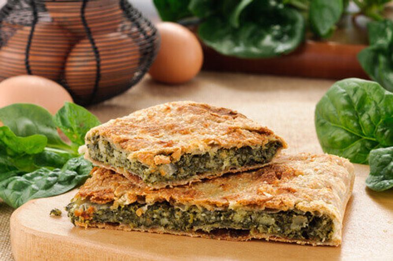 Erbazzone, a savory spinach pie with cheese served on a wooden board.
