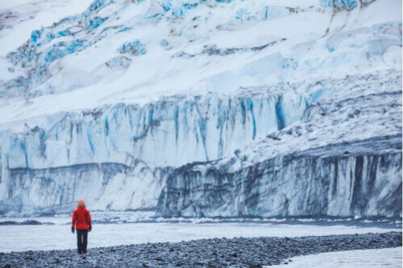 A person walks in front of a glacier in the Shetland Islands, Antarctica.