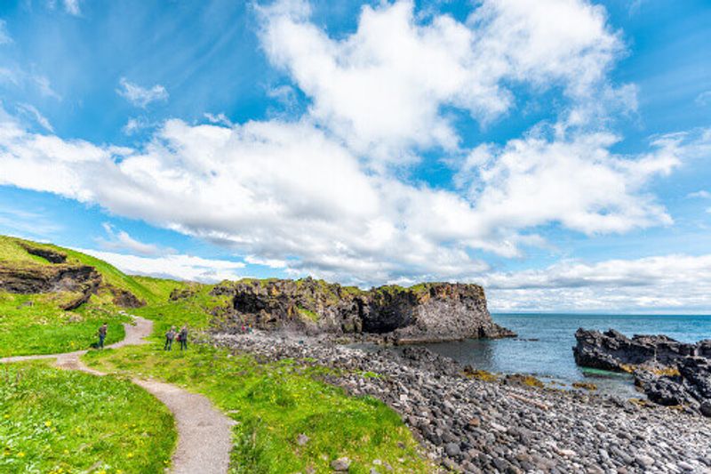 Tourists on a landscape trail, hiking with a view of the rocky beach in Hellnar National Park.