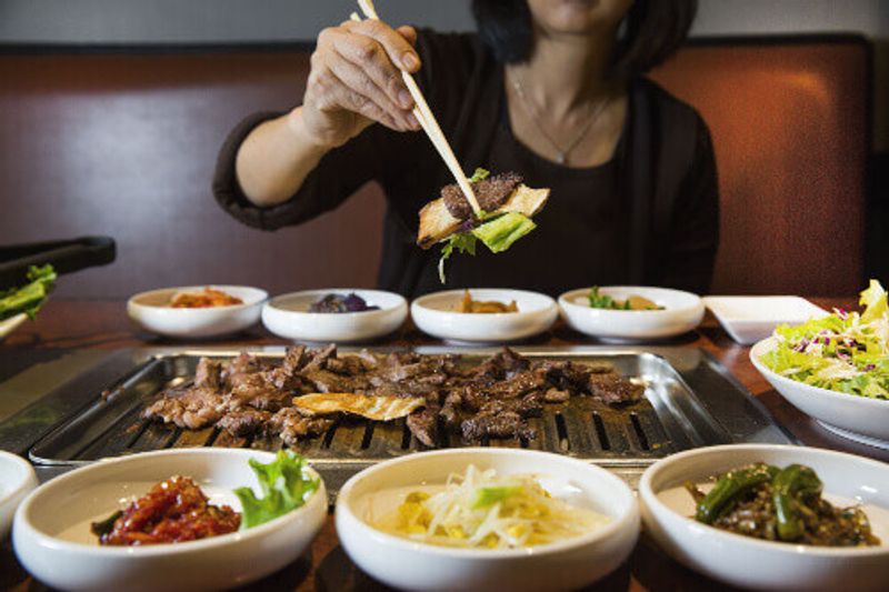 Korean BBQ raw beef on the grill with pickled banchan vegetables.