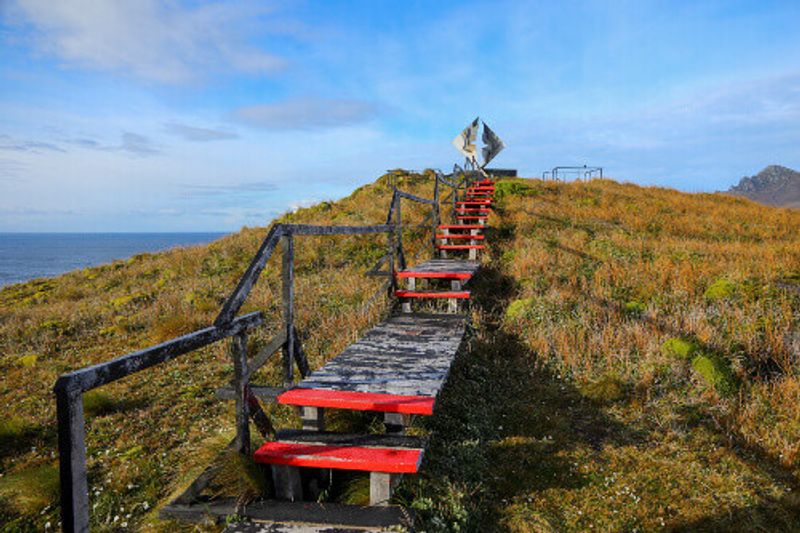A wooden path leading towards the Cape Horn Memorial Sculpture on Cape Horn Island in Chile.