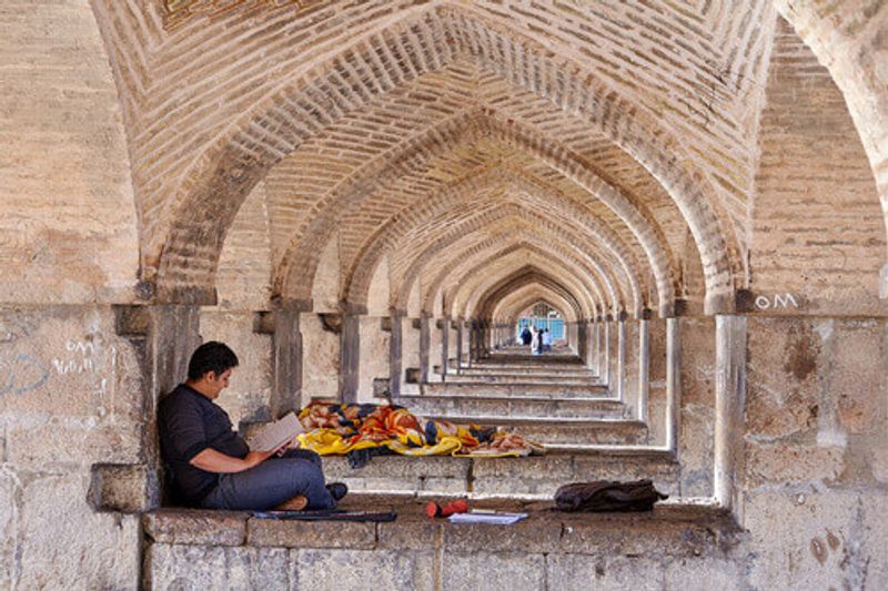 A young man reads notes in a notebook under Khaju Bridge in Esfahan, Iran.