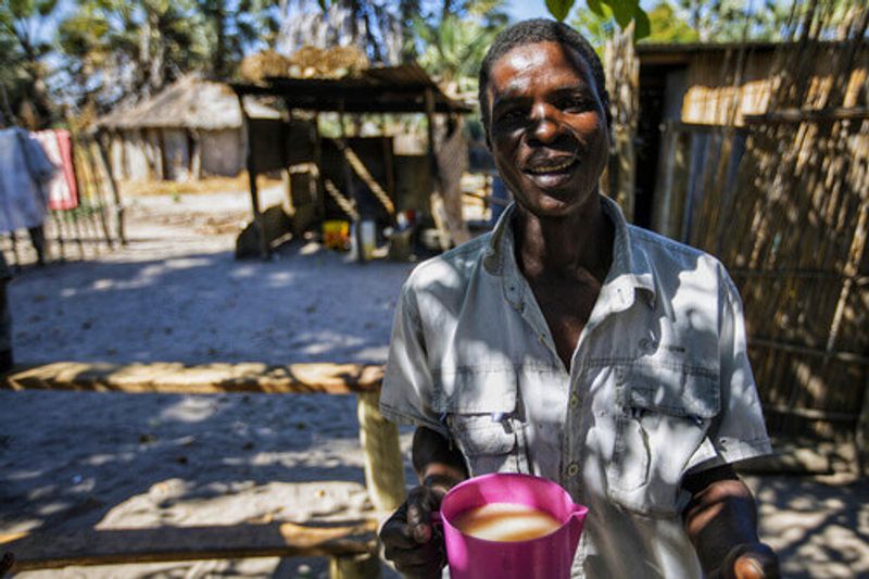 Local man holding a cup of homemade beer at the front of his hut near Okavango Delta in Maun.