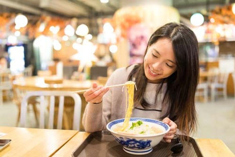 A woman eats a bowl of Ramen with chopsticks in Japan.