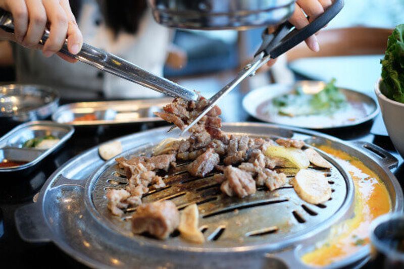 Cutting grilled pork meat in a grill at a Korean restaurant.