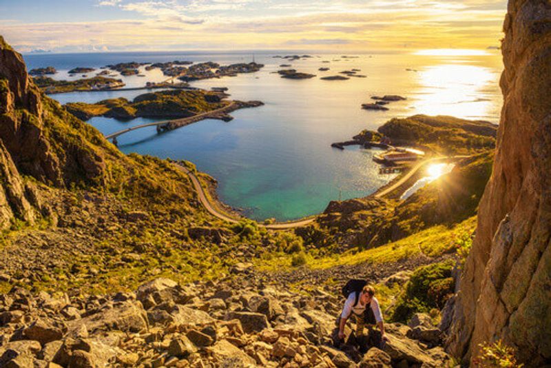 Hiker going to the top of Mount Festvagtind with views over the village of Henningsvaer in Lofoten Islands, Norway.