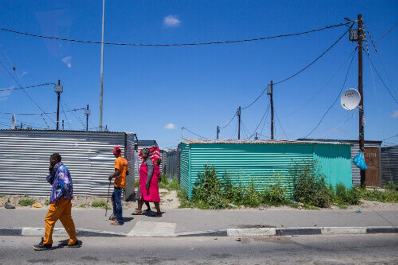 South African people walking down the street with corrugated metal sheets turned into homes.