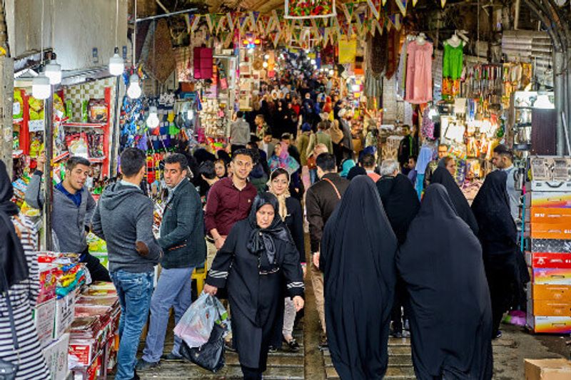 Iranian men and women wearing a hijab in a bustling bazaar in Tehran.