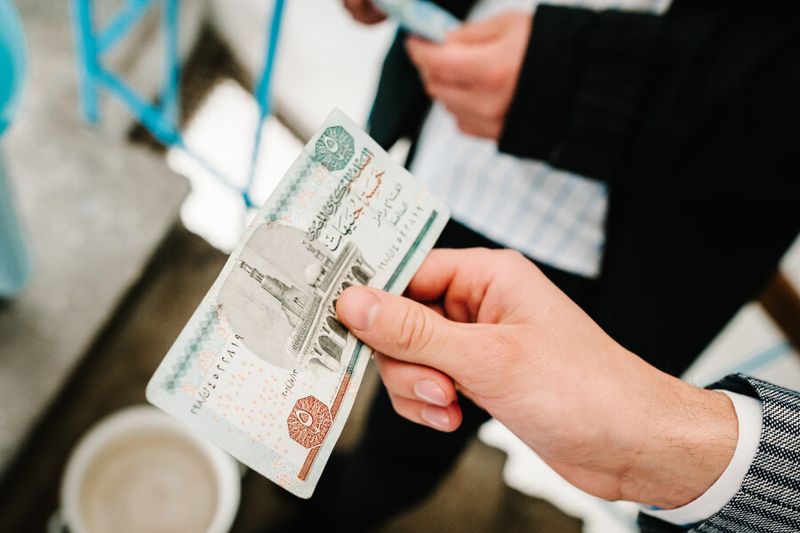 Man holding a Five Egyptian Pound at a cash register.