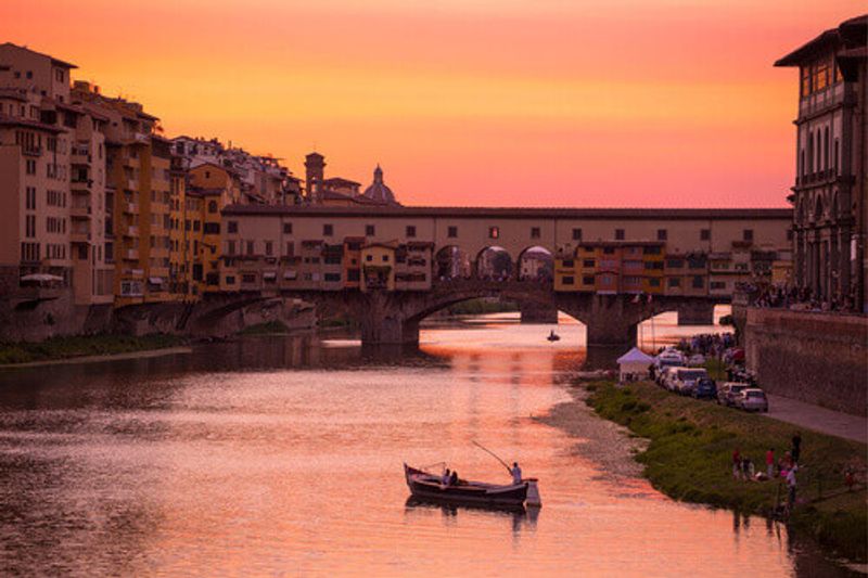 The Ponte Vecchio Bridge and vintage Barchetto Boat near the Arno River in Florence.