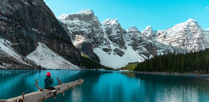 A traveller takes in the stunning Moraine Lake with snow-covered Rocky Mountains in Banff National Park