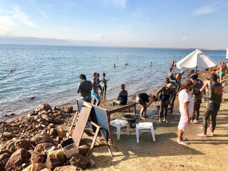 Tourists floating on  salty water and applying mineral mud to their skin at a hotel beach on the Dead Sea.