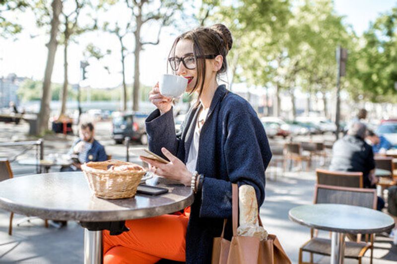 A young woman is having breakfast with coffee and a croissant sitting outdoors at a French Cafe in Lyon City, France.