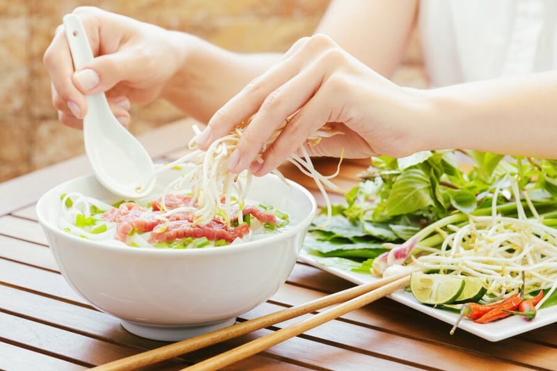 A woman sprinkling bean sprouts on Pho Bo in a cafe of Southern Vietnam.