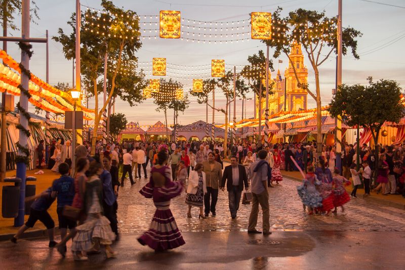 People walk on a lantern-lined street to celebrate the Seville April's Fair during sunset.