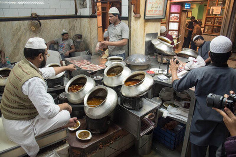 A local man cooks curry in an old wok in a street market of Delhi, India.
