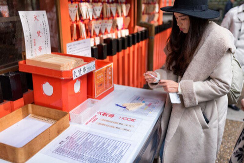 A woman writes a wish on a fox ema plaque in Kyoto, Japan.