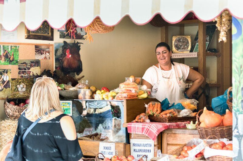 A friendly seller speaking and smiling to a customer at a grocery store in a public market in Split.