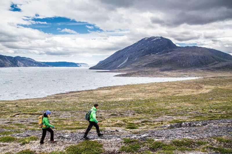 Two tourists wearing winter clothes, walking in the cold vastness of Greenland.