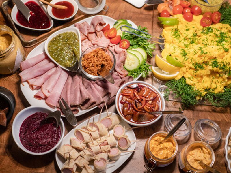 A variety of foods, including an assortment of cold cuts and herring and sauces and scrambled eggs.