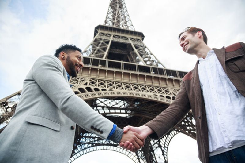 People shake hands in front of the iconic Eiffel Tower.