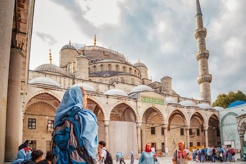 The view of the Blue Mosque with a female tourist wearing blue hijab watched as people go in and out