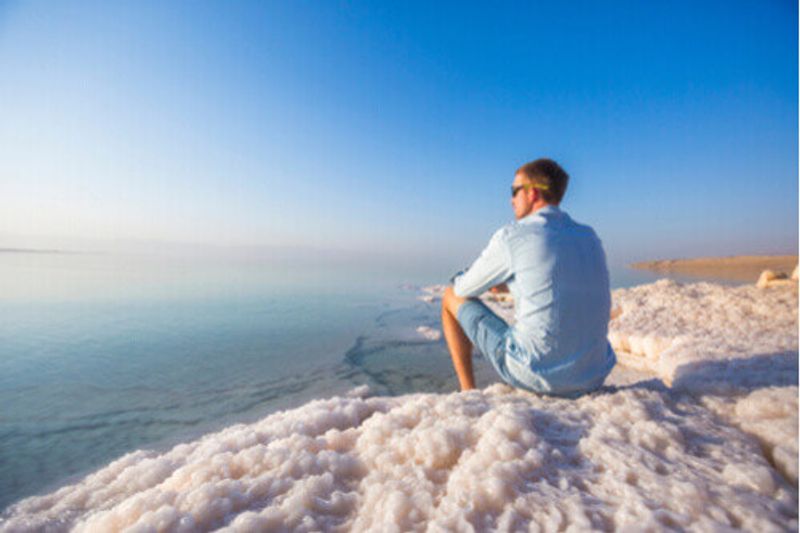 A male tourist sits on the shore of the Dead Sea.