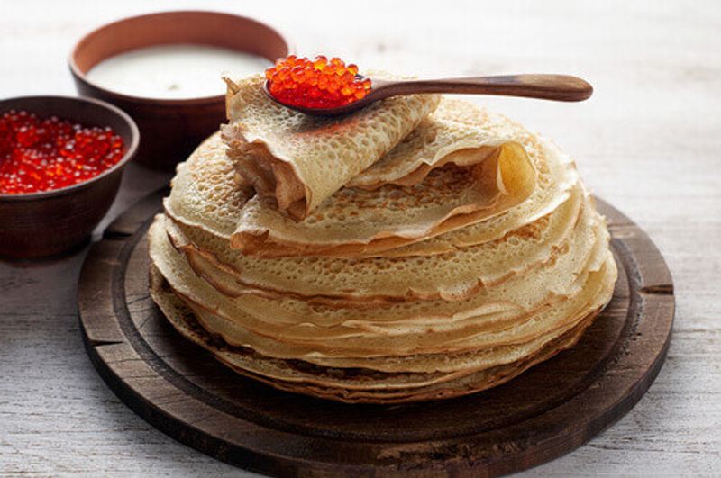 Stack of russian thin pancakes, or Blini, served with red caviar and fresh sour cream.