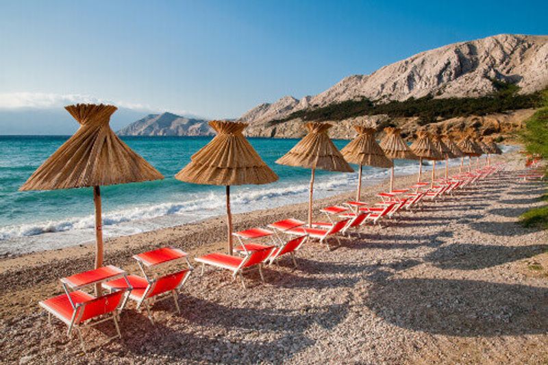 Sunshades and orange deck chairs on a beach at Baska in Krk.