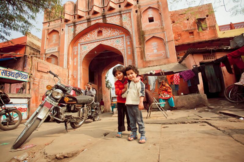 Children pose in front of a traditional Jaipur pink gate.