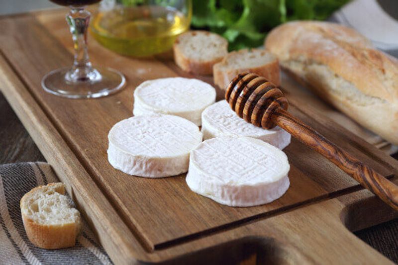 Soft French goat cheese Rocamadour, bread, honey, lettuce and glass of red wine on display