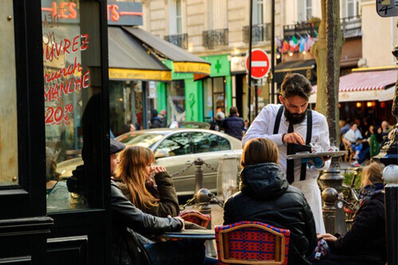 A waiter serves customers at traditional outdoor Parisian Cafe on Rue Mouffetard in Paris, France.