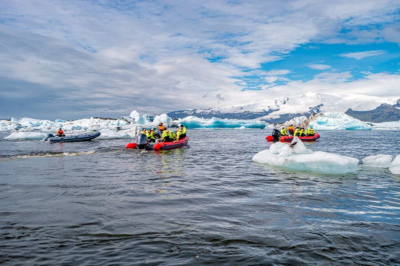 A small boat tour with tourists taking photos of glaciers and icebergs at a lake in Jokulsarlon